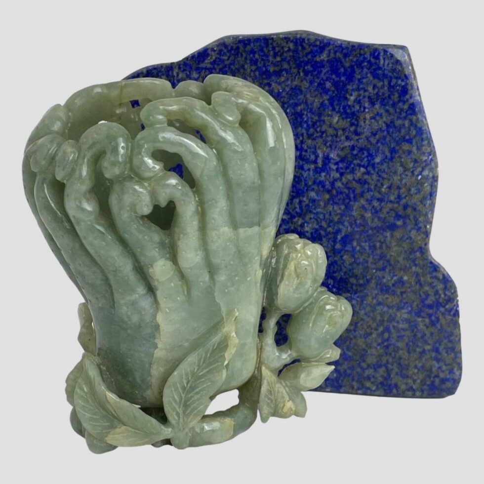 Photo of the jadeite calligraphy water pot this time displayed with the less decorated side on display. The rock of lapis is protruding to the right behind the pot.