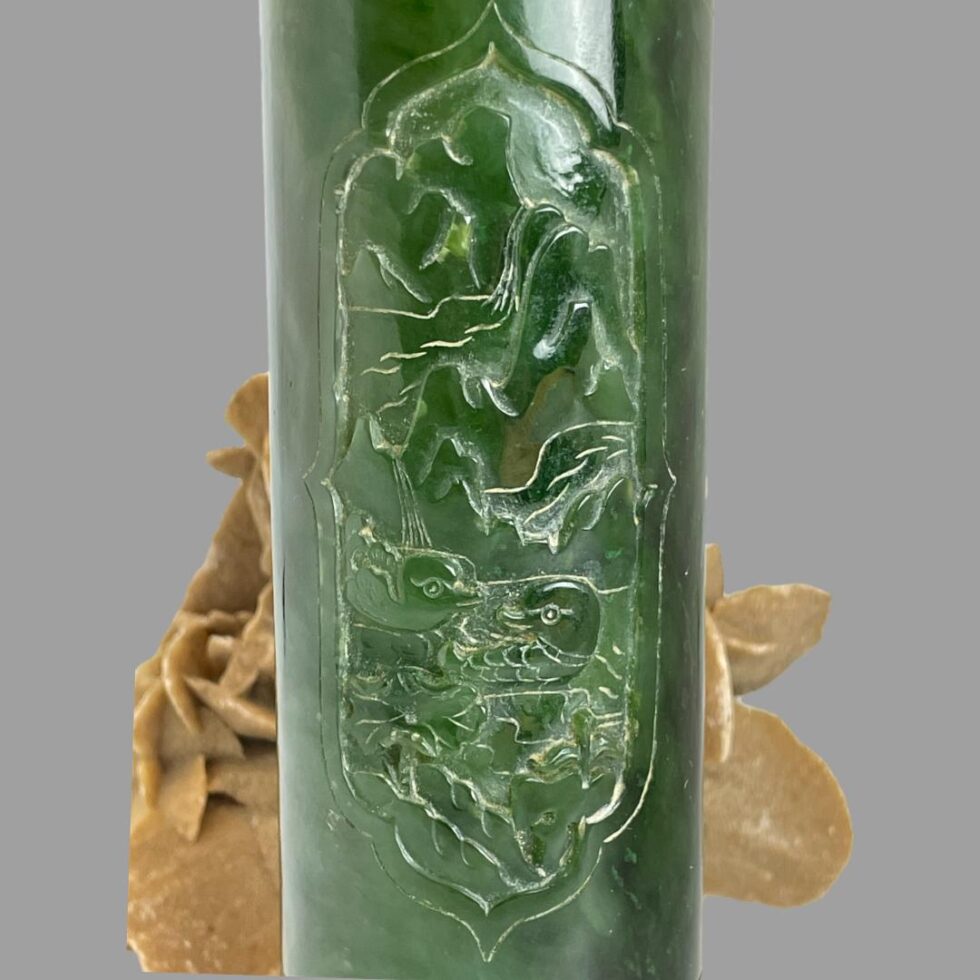 Close up photo of the carved scene of the spinach green pot showing the mountain range in the background, waterfall to the left and a pair of ducks enjoying a swim. The desert sand rose is still in the background.