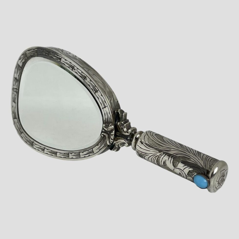 Main photo of 800 silver vanity mirror displayed upright on its side with the handle in the bottom right corner. There is a turquoise blue coloured stone at the tip of the handle which is where the lipstick holder slides out and also doubles as lipstick pusher upper. The rest of the vanity mirror will unfold in coming photos!