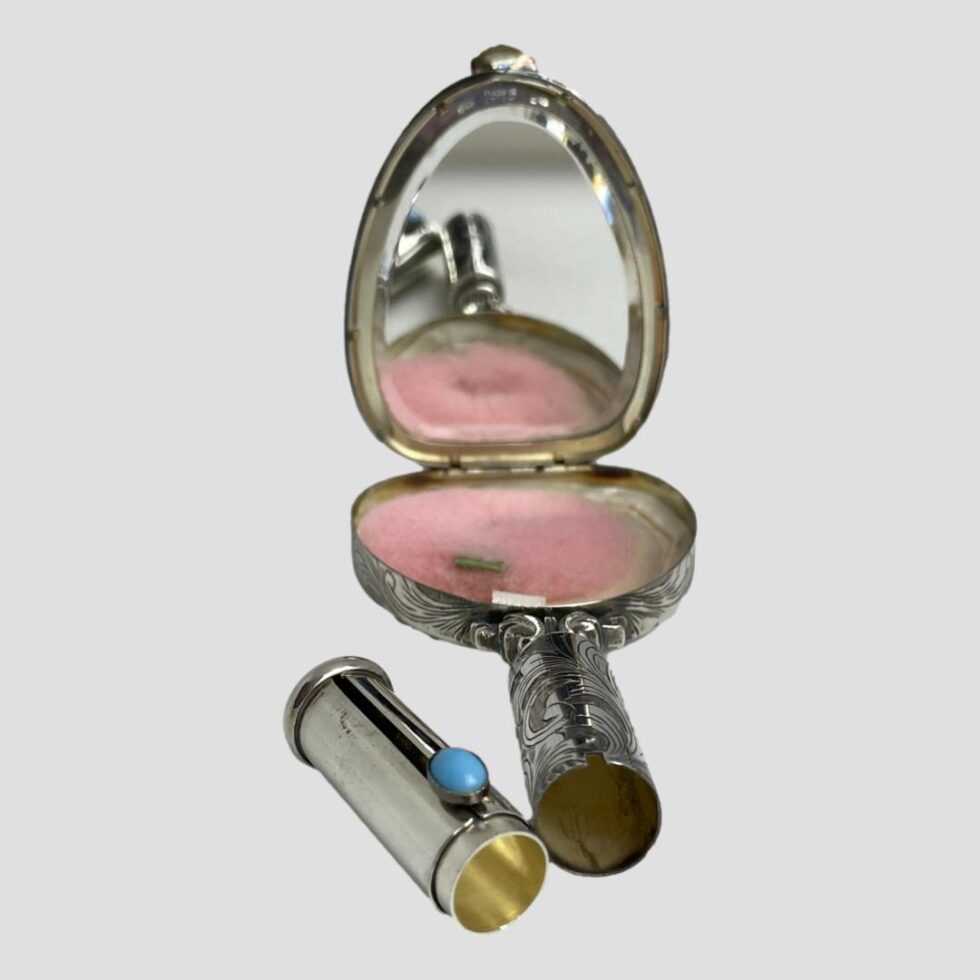 Photo of vanity mirror with lipstick holder removed and placed to the left side. The mirror is displayed with the handle in the centre foreground and the pink powder puff in place. The lipstick holder has been pushed all the way up to show the area where lipstick would be put.