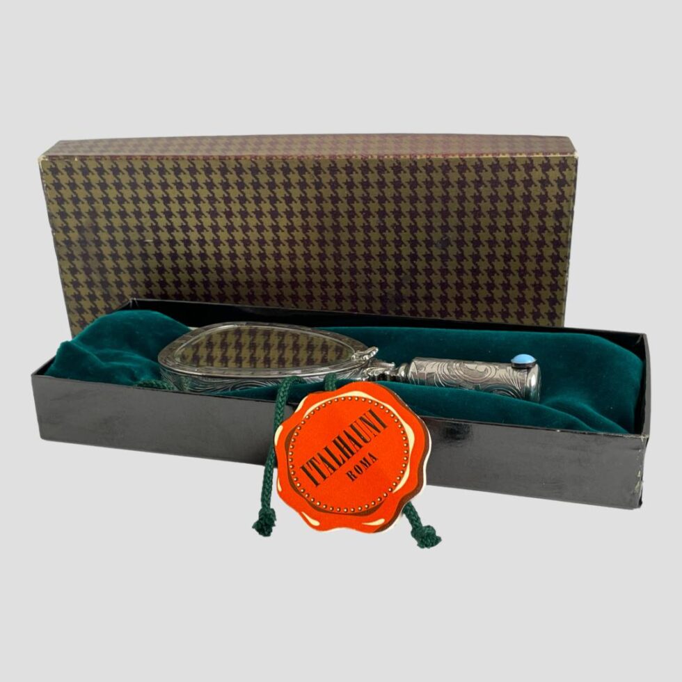 Photo of 800 silver vanity mirror displayed inside its original box laid on top of the green velvet cover. The original label is still attached to the drawstring of the bag which says Italhauni Roma. The opposite side says Made in Firenze.