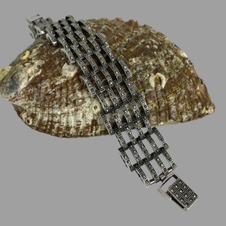 Main photo of modern silver marcasite bracelet draped over a shell with the opening clasp end in the bottom right foreground.