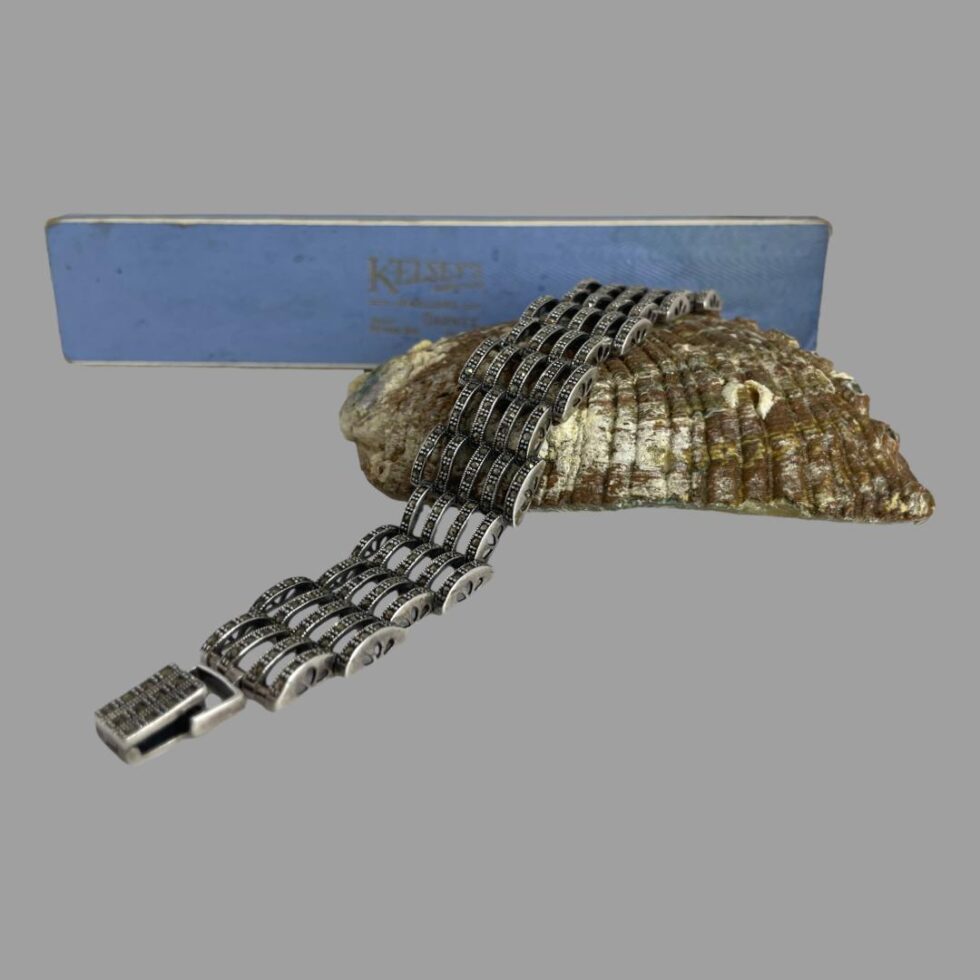 Photo of bracelet still displayed across the back of a shell. The box included for the bracelet is in the background - light blue. Some staining to the right on lid & foxing marks.