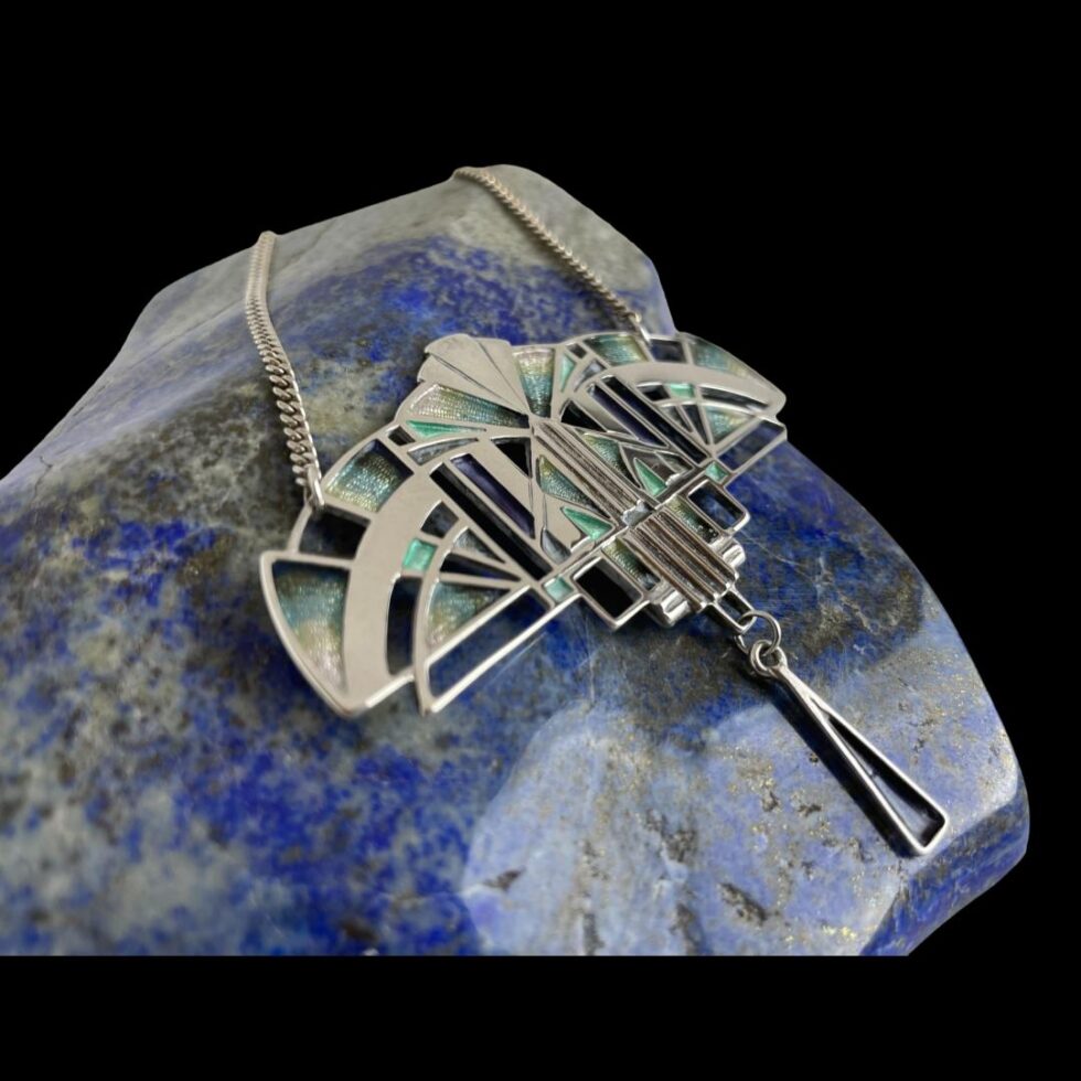 Photo of Deco style silver necklace still displayed on a rock of polished lapis this time with the pendant front facing to the right.