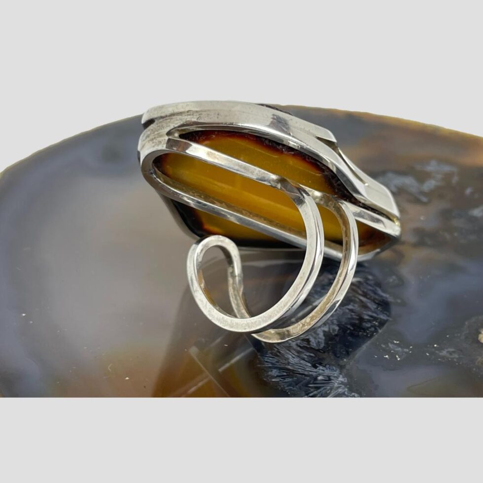 Photo of back of large amber ring angled to show the open double band which is made up of 2 thinnish bands coming round from the front setting. These bands appear separate but are connected at the ends in a curve shape. There is probably a little room for adjustment if needed.