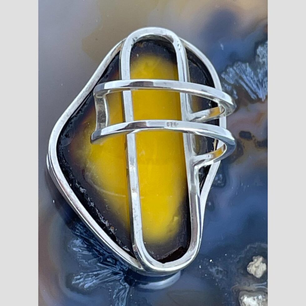 Photo of large Baltic amber ring displayed face down showing the intricate silver framework holding the amber and the double band. The 925 hallmark is just visible on the lower band.