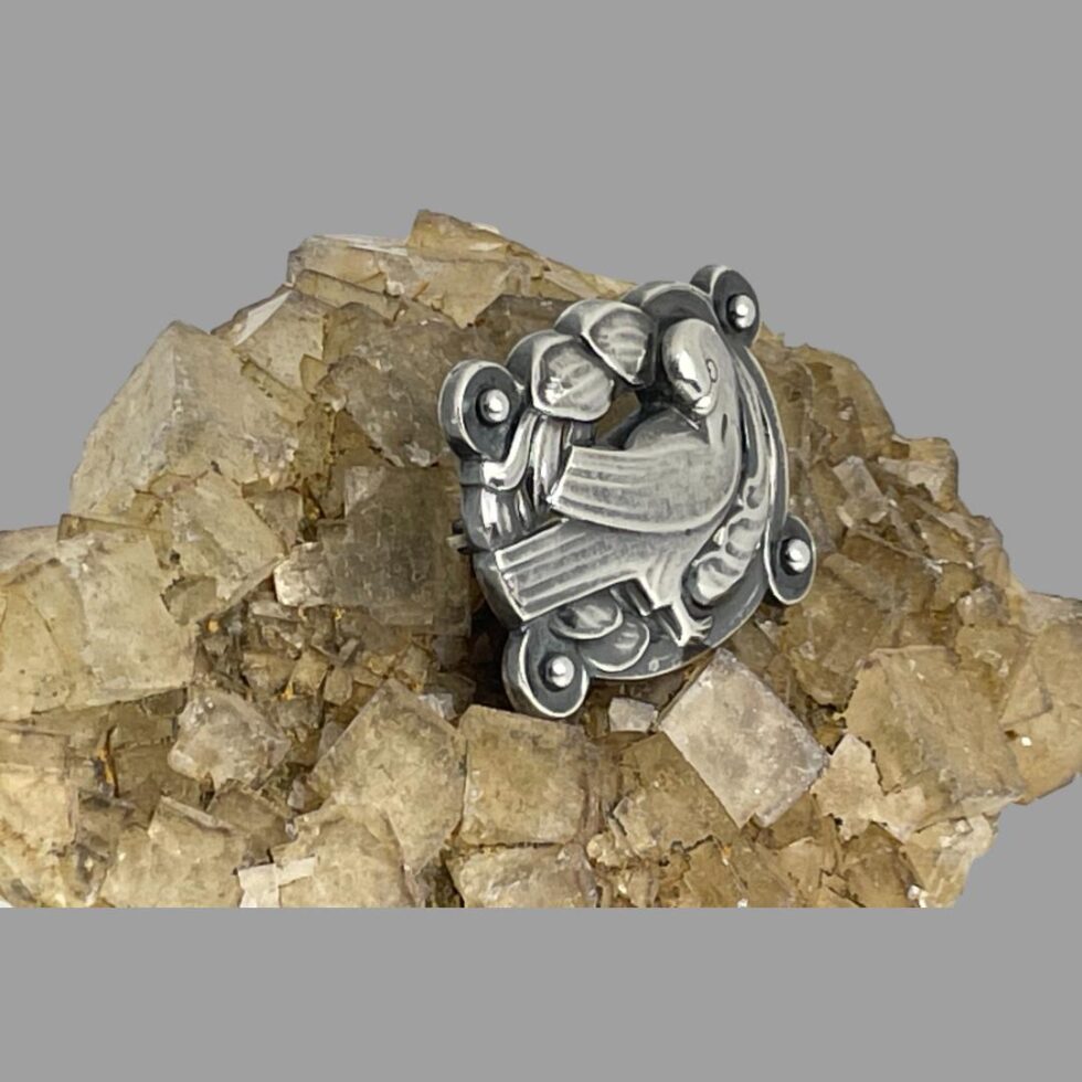 Photo of Jensen dove brooch still on top of river quartz this time with the brooch front facing to the bottom right corner.