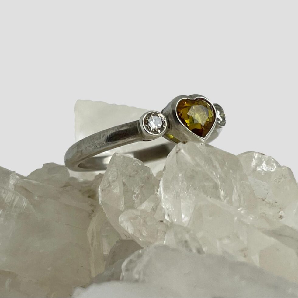 Photo of yellow sapphire diamond ring still on top of a rock of natural quartz crystal this time with the ring front facing upward to the top right corner of photo.