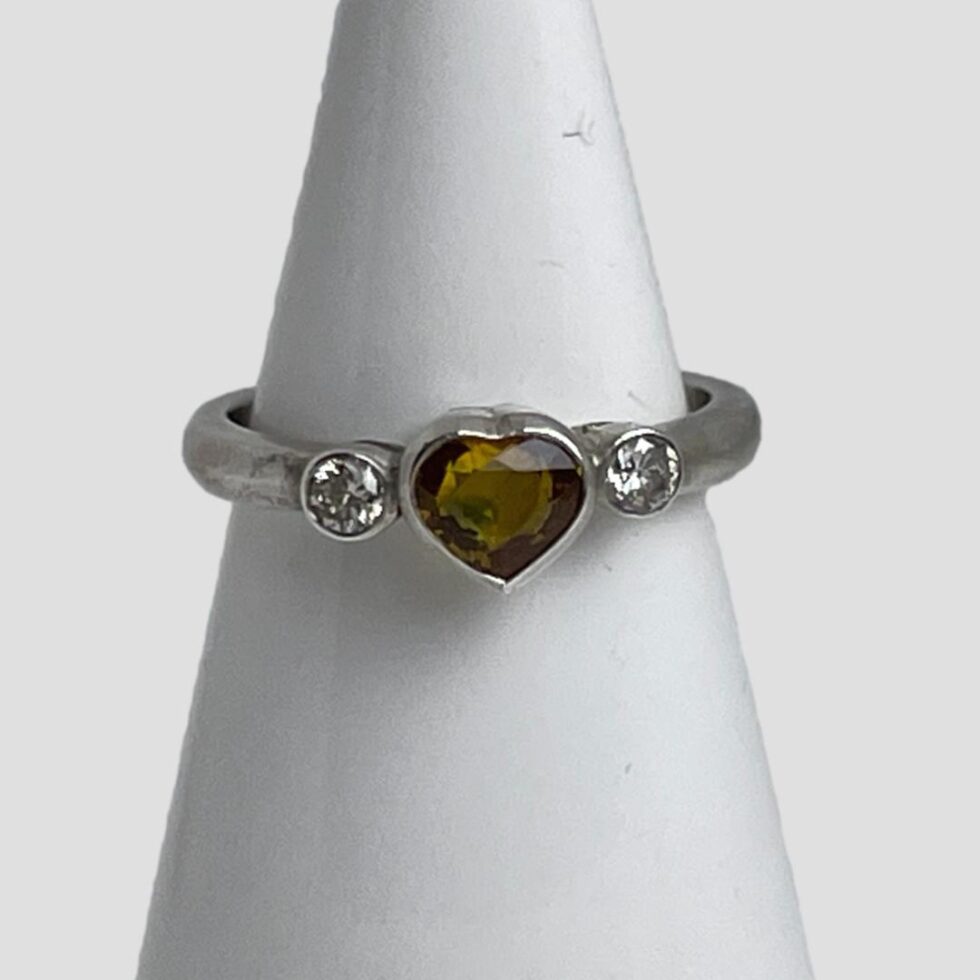 Photo of yellow sapphire heart ring displayed on a white cone shaped stand with the ring front forward facing.