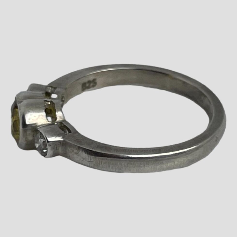 Photo of yellow sapphire heart ring displayed on a flat surface with the ring front facing left. The 925 hallmark is visible to the inside band.