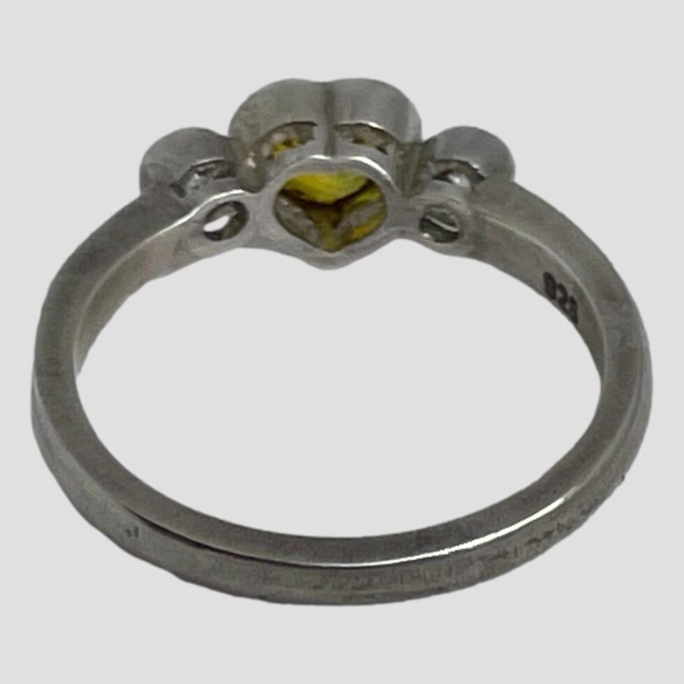 Photo of the back of the yellow sapphire heart ring displayed on a flat surface with the back band in the foreground. The back setting for the precious stones is visible.