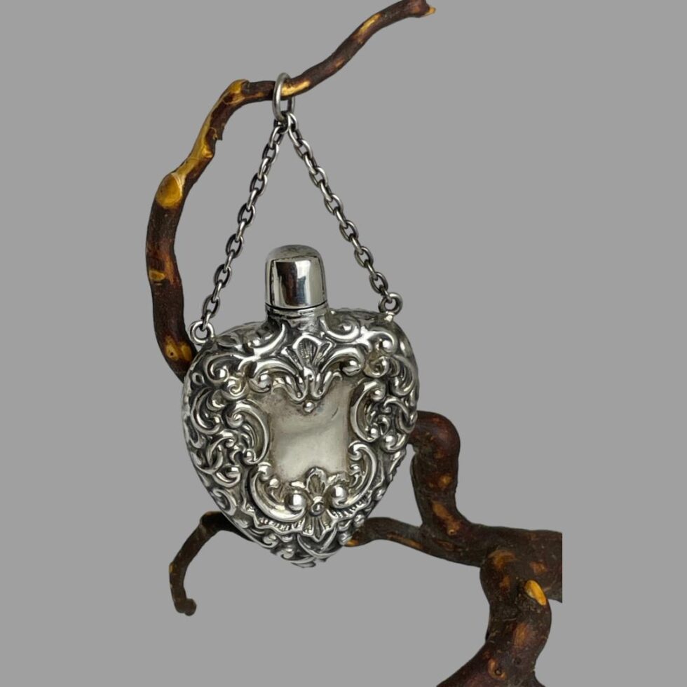 Another photo of the silver heart scent bottle still hanging from a twig this time with the front slightly angled to the right.