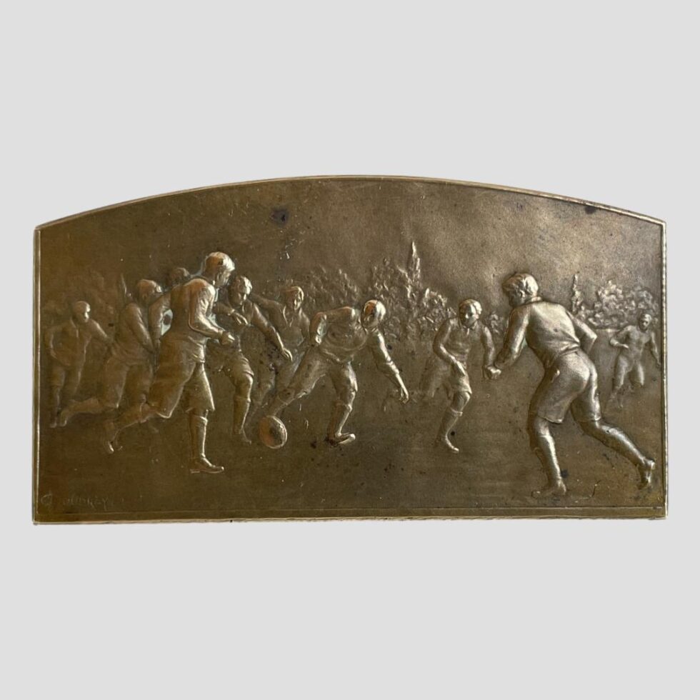 Main photo of French bronze football medal displayed with the football players in mid play on display. The players stand out in relief and are dressed in knee length shorts, long sleeved tops and knee high socks - a telling confirmation of the era!