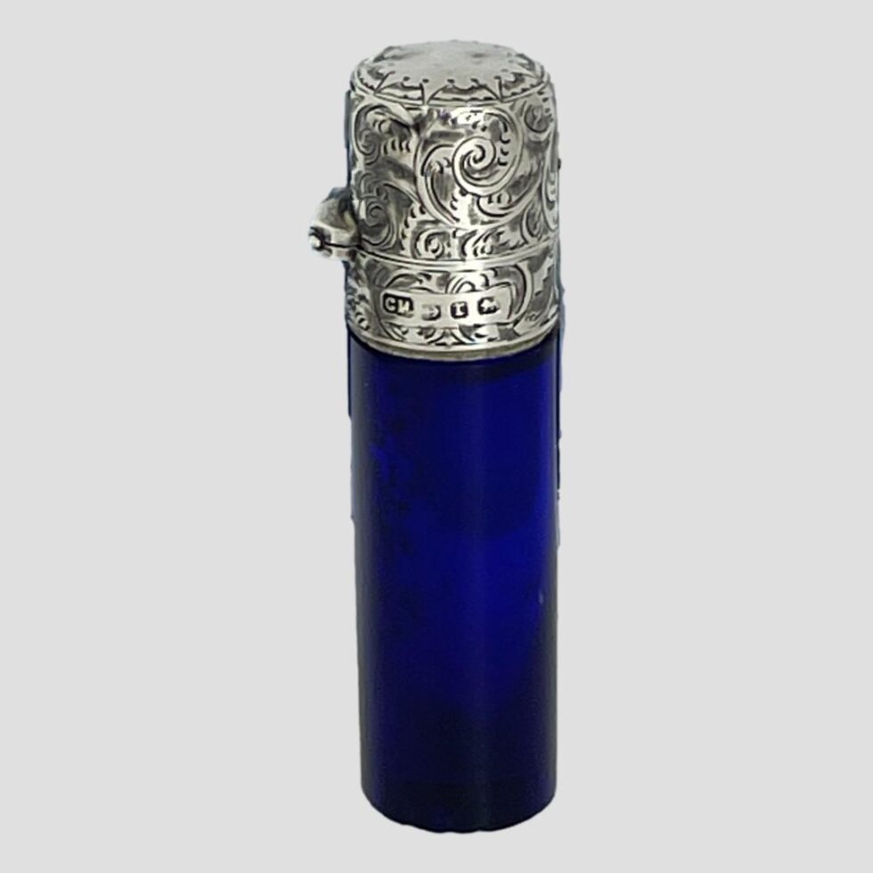 Photo of antique portable scent bottle displayed from an eye level side angle. The hinge for the top is visible on the left and the full hallmark is also visible on the side .