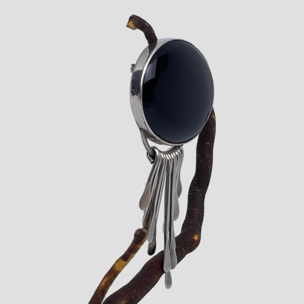 Photo of the onyx brooch pendant still displayed hanging from the twig this time with the brooch front facing to the right to show the depth of the piece.