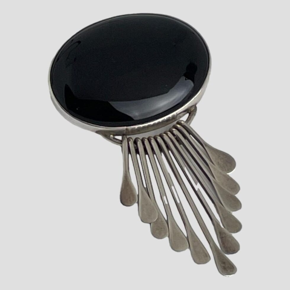 Photo of Mexican onyx brooch pendant displayed on a flat surface with the silver strands fanned out but together.