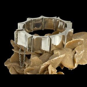 Main photo of Taxco concave rectangle bracelet displayed on top of a rock of natural desert sand rose. The whale tail clasp is visible to the left and the safety chain hangs down below. There is a heavy metal punk like look about this piece of substantial Mexican silver jewellery.
