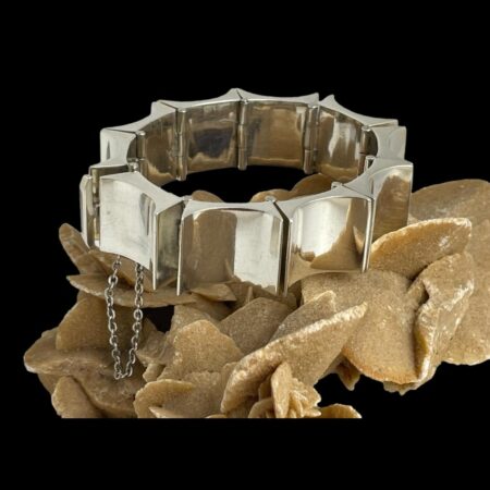 Main photo of Taxco concave rectangle bracelet displayed on top of a rock of natural desert sand rose. The whale tail clasp is visible to the left and the safety chain hangs down below. There is a heavy metal punk like look about this piece of substantial Mexican silver jewellery.