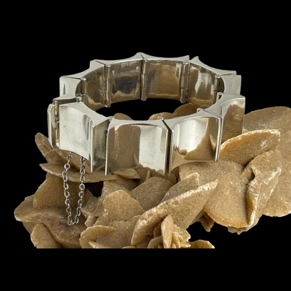 Main photo of Taxco concave rectangle bracelet displayed on top of a rock of natural desert sand rose. The whale tail clasp is visible to the left and the safety chain hangs down below. There is a heavy metal punk like look about this piece of substantial Mexican silver jewellery.