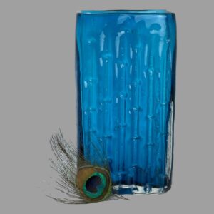 Main photo of Whitefriars blue bamboo vase displayed with the bamboo side on show. A colourful tip of a peacocks feather is to the bottom left for display only. The kingfisher blue colour of this vase is much sought after from the Whitefriars range of glassware.