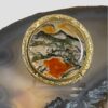 Main photo of vintage moss agate brooch displayed on a slice of natural agate. The brooch front is forward facing.