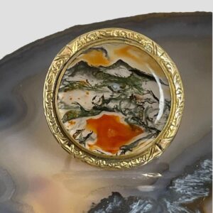 Main photo of vintage moss agate brooch displayed on a slice of natural agate. The brooch front is forward facing.
