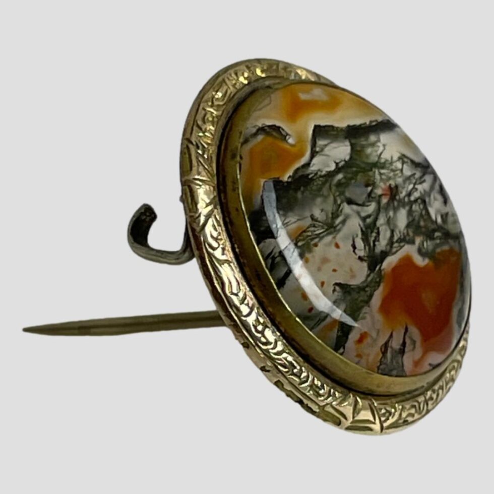 Photo of moss agate brooch this time propped upright by its own pin with the brooch front forward facing.