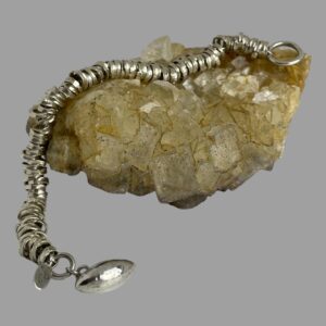 Main photo of modern silver rings bracelet displayed draped over a rock of natural river quartz. The half rugby ball end of clasp is in the bottom left foreground.