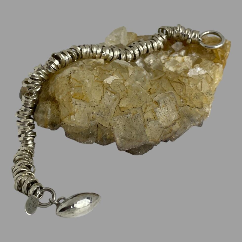Main photo of modern silver rings bracelet displayed draped over a rock of natural river quartz. The half rugby ball end of clasp is in the bottom left foreground.