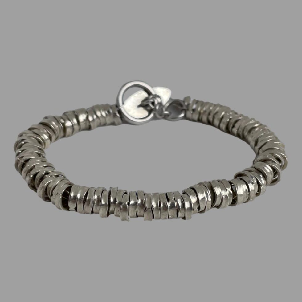 Photo of modern sterling silver rings bracelet displayed on a flat surface with the clasp closed and in the centre background. The silver ring beads are shown in close up in the foreground.