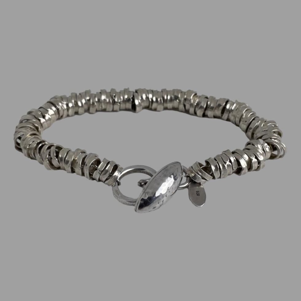 Photo of the modern sterling silver rings bracelet displayed on a flat surface this time with the clasp area in the centre foreground. The clasp is shown closed and the 925 hallmark on the back of makers tag is just visible.