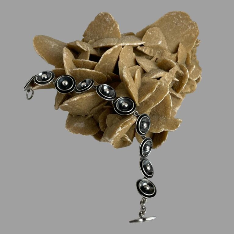 Main photo of Modernist Danish silver bracelet displayed draped across a rock of desert sand rose with the whale tail clasp end in the centre foreground.