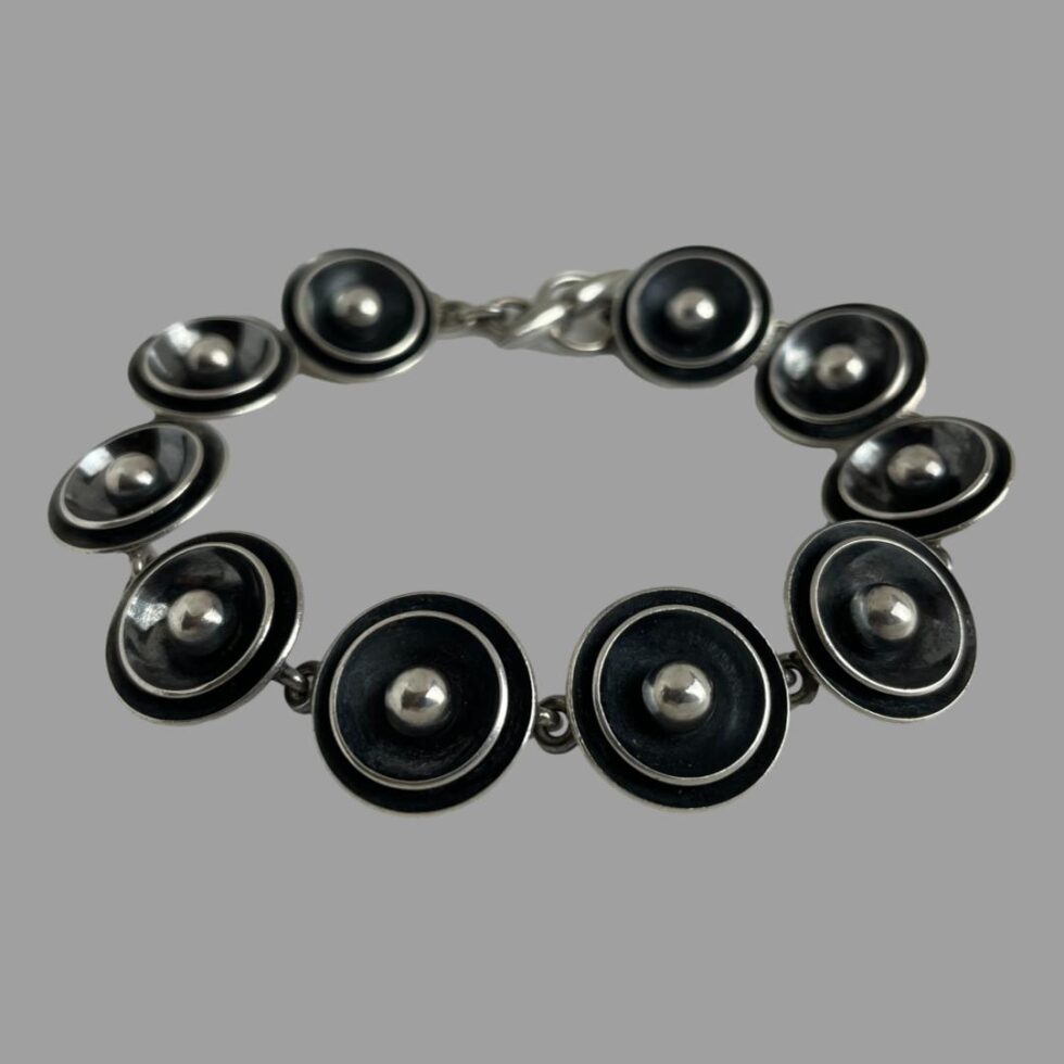 Photo of Modernist Danish silver bracelet displayed on a flat surface with the clasp end in the centre background. The front row of the disc panels are laid facing outward while the disc panels at the back are laid facing inward.
