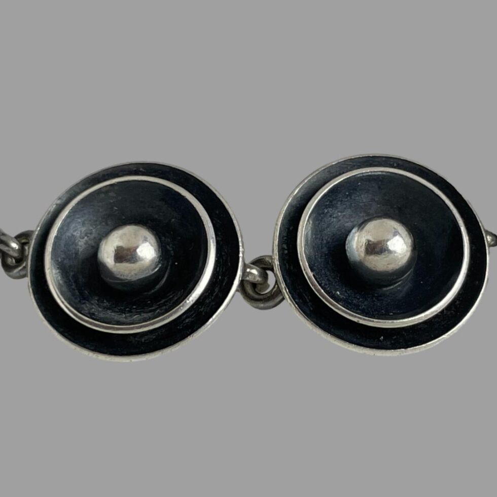 A close up photo of 2 of the disc panels. The discs have a silver ball to the centre with a shallow 'bowl' around it to the centre in oxidised silver which is black. The rim of that inner 'bowl' is silver. The outer 'bowl' is also in oxidised black silver to create a lovely 3D effect with depth. Making for a very striking design detail.
