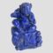 Main photo of vintage carved lapis figural sculpture with its front forward facing. The figure, a young child like male is sat on a rock being lapped by the sea with a large fish possibly a carp, leaping from the water to the bottom left. The boy has a raised left hand (right in the photo) with palm forward facing and his right arm is holding a ring from which a piece of cloth is attached. The boys hair is bunched up on the sides into tight rings and he wears a neck band. Believed to be a good luck ornament.