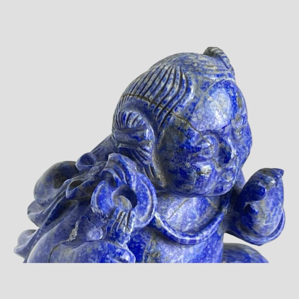 Close up photo of the figures head looking from the right side angle and down. The natural crack in the lapis stone is visible to the top of his head and the repair is visible to the left of his hand. There is a small chip also visible on the ring holding the cloth.