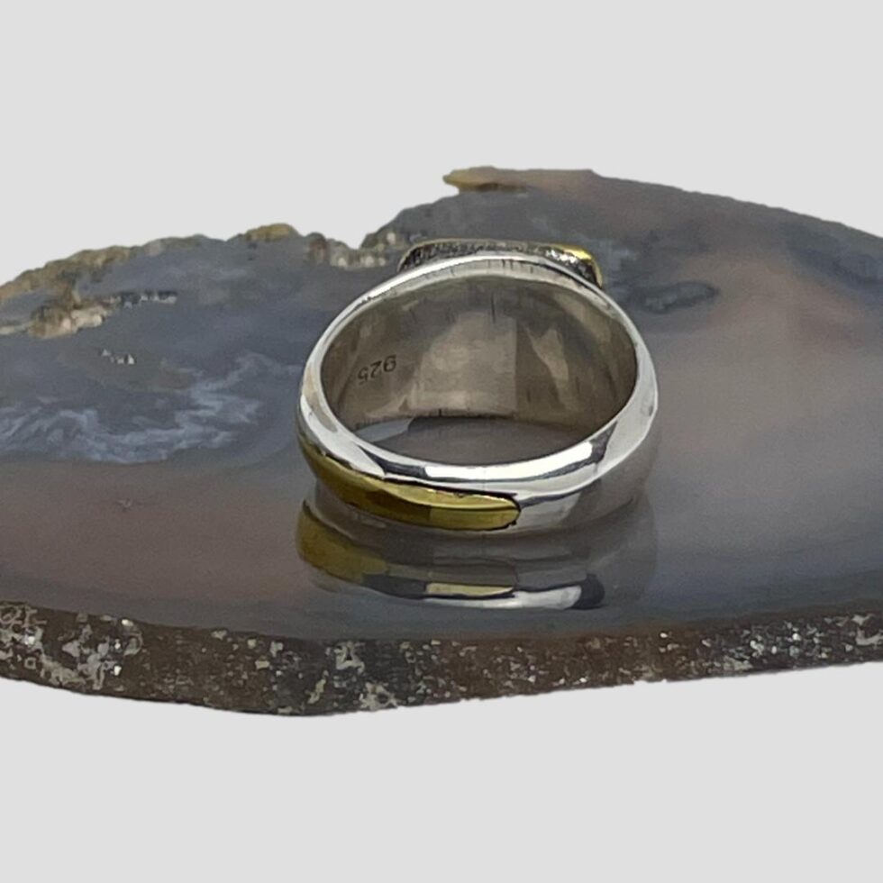 Photo of the back of ring showing the area behind the fragment which is sealed and solid silver also the end tip of the long gilt metal strip.