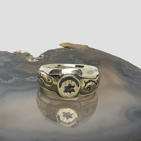 Main photo of upcycled Medieval fragment ring displayed on top of a slice of natural agate with the ring front facing forward. The crescent moon is set across the top of the circular bronze centre with the star underneath it. The bronze fragment extends on either side to make the shoulders. These areas have some embossed detail of possibly vines. The band is in solid sterling silver and the plainness of it compliments the Medieval bronze fragment perfectly.