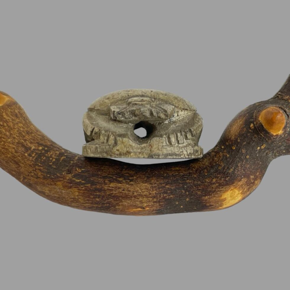 Photo of scarab beetle bead leaning on cherry tree twig with the head of the beetle in the foreground. We are looking through gap in the bead.
