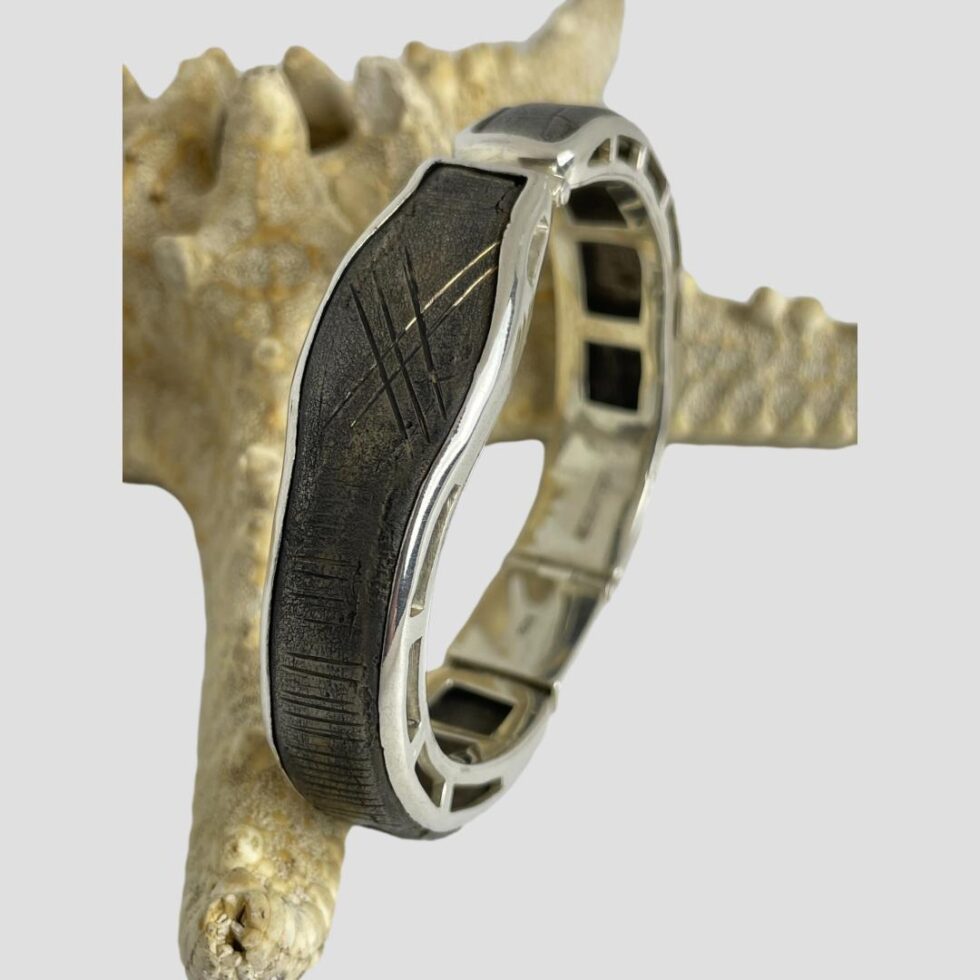 A close up photo of the 'head' area of the bracelet. The bracelet is propped up on its side (leaning against the starfish) with the head area in the centre foreground. The hallmark is blurred but just visible to the inside band.