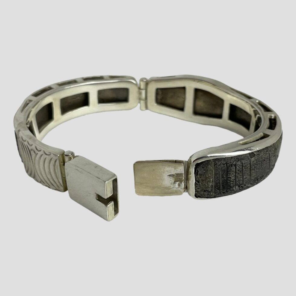 Photo of Viking snake bracelet displayed laid on a flat surface with the clasp in the centre foreground and shown open with the 2 ends close together.. The sterling silver frame work that houses the original snake bracelet is clearly displayed.