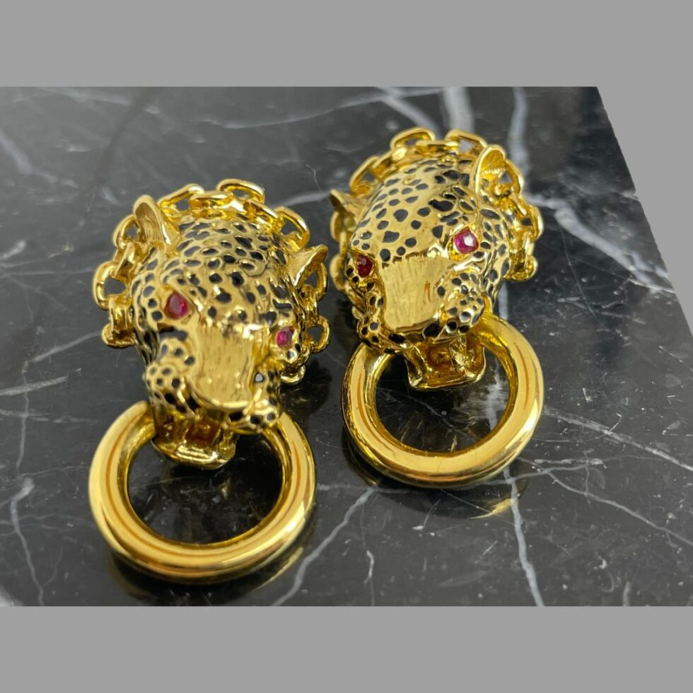 Close up photo of the leopard door-knocker earrings displayed on a block of black marble. Both earrings are forward facing. The gilt is in excellent condition and the red eyes and black spots add a fierce quality of excellence.