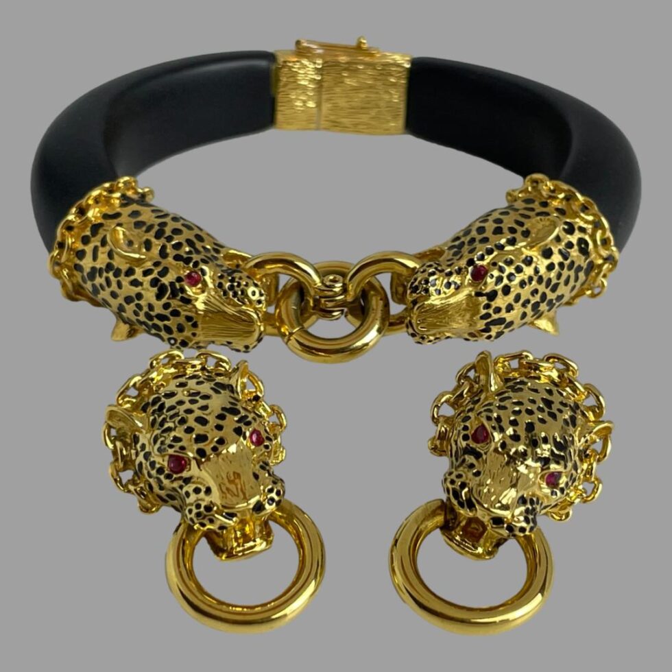 Photo of leopard door-knocker jewellery set displayed on a flat surface against a grey background. The bracelet is set in the background with the leopard heads front of bracelet in the foreground and the earrings are laid in the foreground side by side.