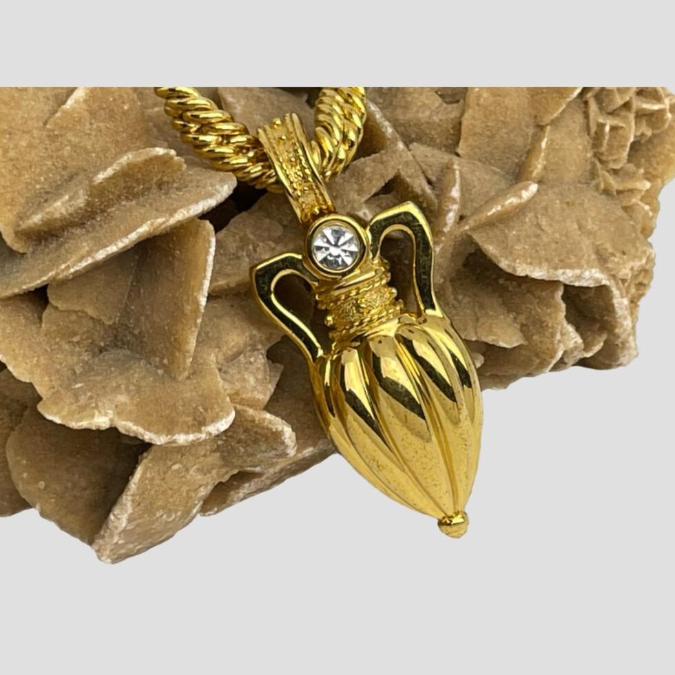 Close up photo of the front of amphora pendant / brooch. The gilt is in excellent order and the single cut glass piece sparkles like liquid at the mouth of the amphora.
