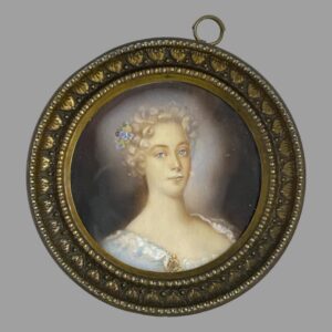 Main photo of antique French miniature portrait displayed upright with the portrait figure looking straight to camera. The ring for hanging the picture is seen off centre and to the right and would be ideal to get it reset. The picture is very securely in place though and may need a professional or at least someone who knows what they're doing to fix it. The lady is wearing a low cut top in pale baby blue with white lace trim. Her curly locks are short in the image and appear white blonde. A small posy with a blue flower sits in her hair which matches the colour of her piercing eyes. There is an evocative feel to this miniature which follows you around the room!