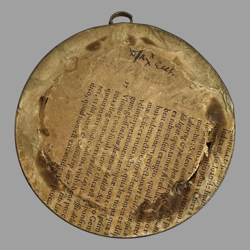 Photo of the back of the antique French miniature portrait. There is some Latin writing on the paper backing and 2 open areas where someone may have possibly tried to straighten the image.