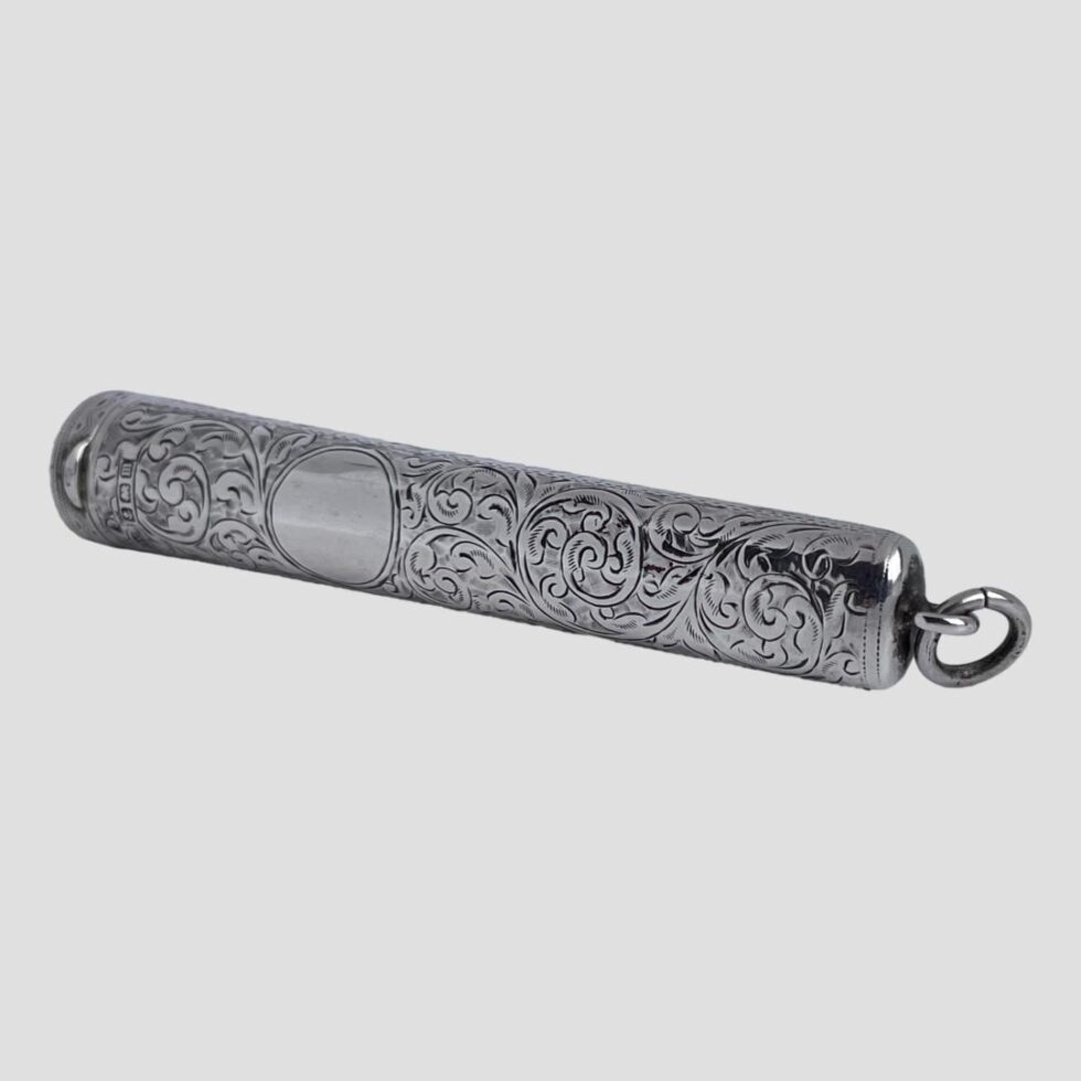 Photo of antique cheroot case displayed on a flat surface this time with the tapered bail end slightly in the foreground on the right. The hallmark is just visible above the cartouche and just below the l;id.