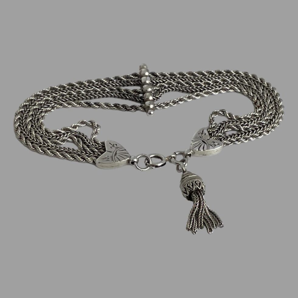 Photo of repurposed Albertina chain bracelet displayed on a flat surface with the clasp, hearts and tassel end in the foreground with the clasp shown closed. The bar separator is in the centre background.