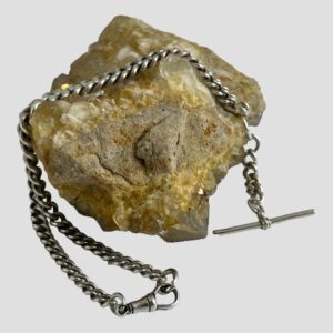 Main photo of repurposed Albert chain necklace displayed draped across a rock of natural river quartz. The T-bar is hanging off the rock on the right and the dog clip clasp shown closed is in the centre foreground.
