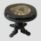 Main photo of Victorian jet miniature table displayed from slight height looking diagonally down at the ammonite in the table top. The jet has been expertly carved with detail to the outer table edge as well as above the table legs. The table is a pedestal variety with a central pillar and 4 feet. There are some signs of wear as well as old repairs. The ammonite in the table top is sectioned and in fine condition.
